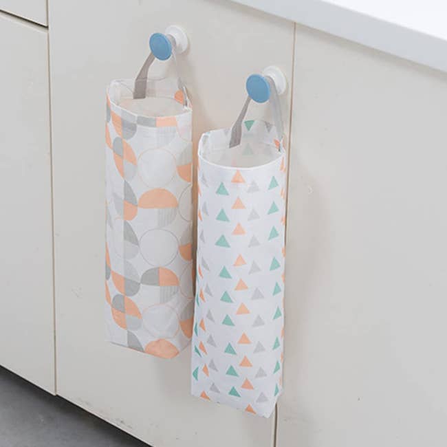 Two  plastic bag holders hanging from a hook on the wall — one is white with green, orange, and grey triangles and the other is white with quartered circle patterns in gray and orange
