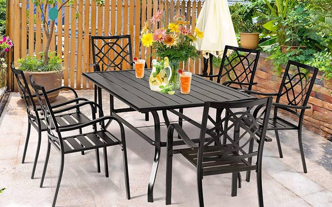 Six black wrought iron chairs around a large rectangular wrought iron table outside in backyard