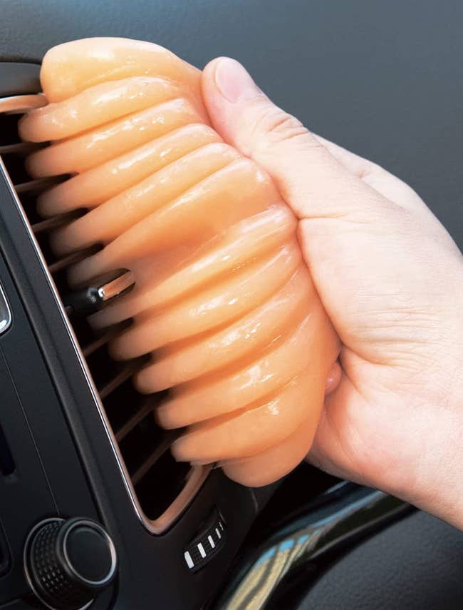 person using an orange putty to clean out vents in the car