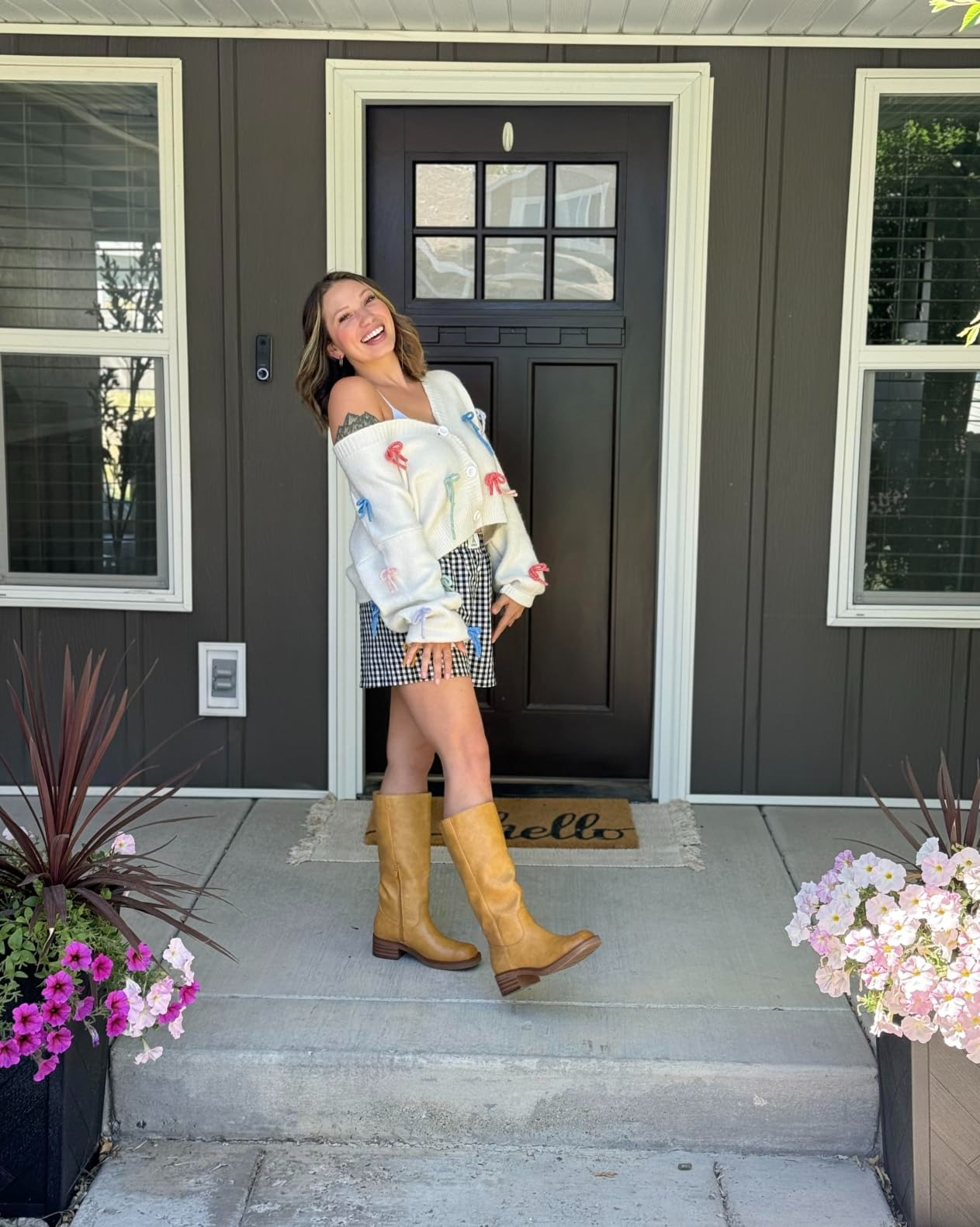 Person smiling connected  a beforehand   porch, wearing an off-shoulder sweater and plaid skirt with knee-high boots, lasting  betwixt  angiosperm  pots