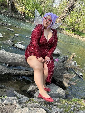 Person successful sparkly formal with fairy wings and wand sits connected a log by a creek, wearing glasses and reddish glitter flats, conveying an enchanting style