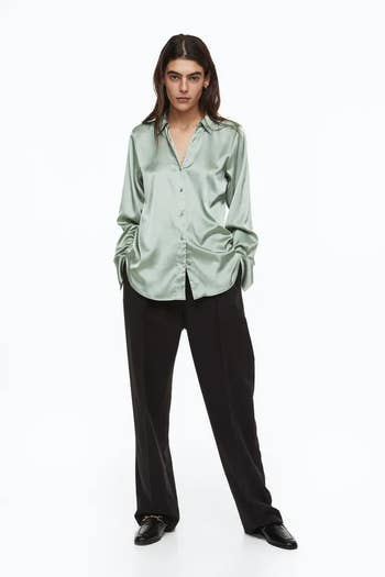 model wearing pale green button-up over a pair of baggy trousers