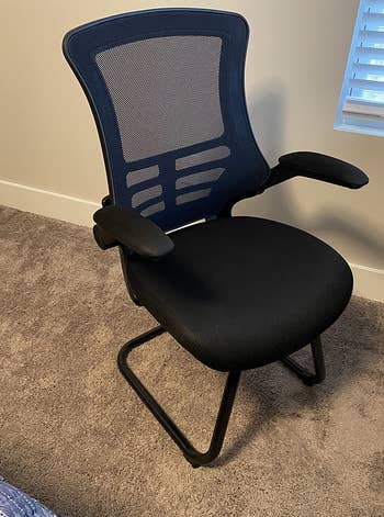 Reviewer image of black mesh chair on brown carpet and tan wall