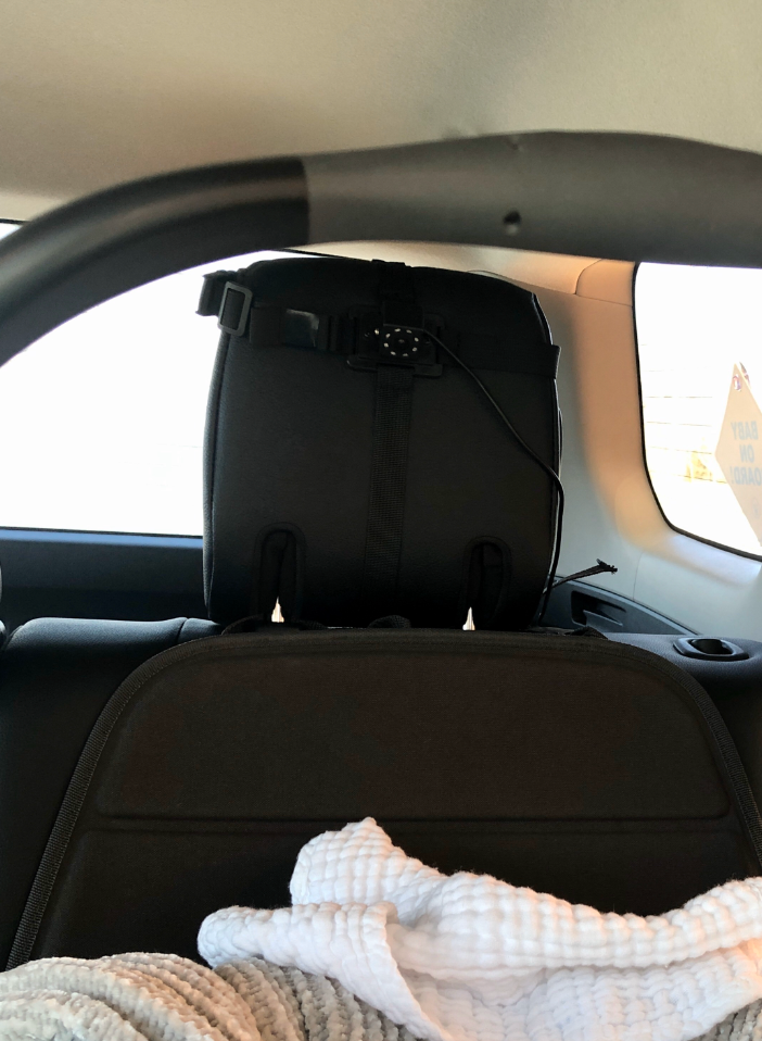 Car backseat with a baby seat and a warning sign on the rear window, partially covered by a white blanket
