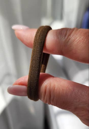 Hand holding a brown hair elastic looped around two fingers, highlighting its texture and stretchiness. Ideal for securing ponytails or updos