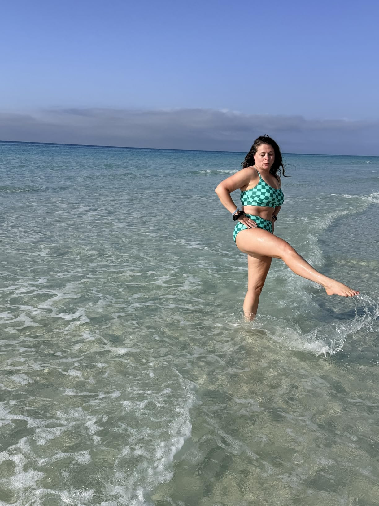 Person successful  a checkered swimsuit playfully kicks h2o  astatine  the beach