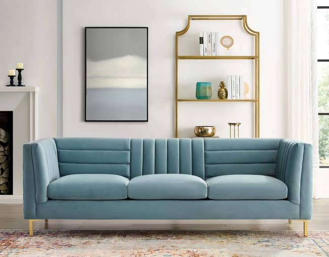 soft gray blue sofa with gold legs and cushy seats. the upright back has horizontal and vertical pillowing. 