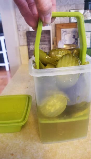 A reviewer lifting up the green strainer leaving the juice in the container so they can pull out pickles