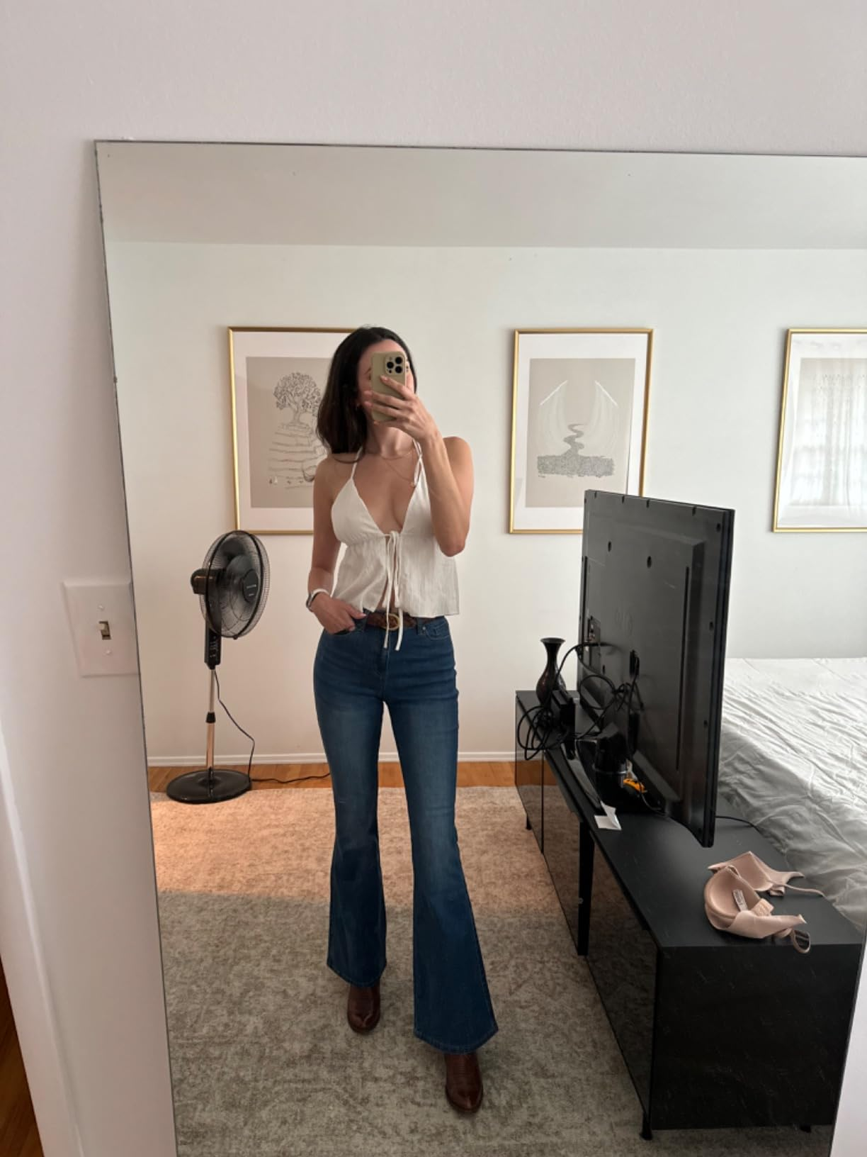 Person successful  a reflector  selfie wears a achromatic  halter apical  and flared jeans successful  a modern   chamber  with minimalist decor