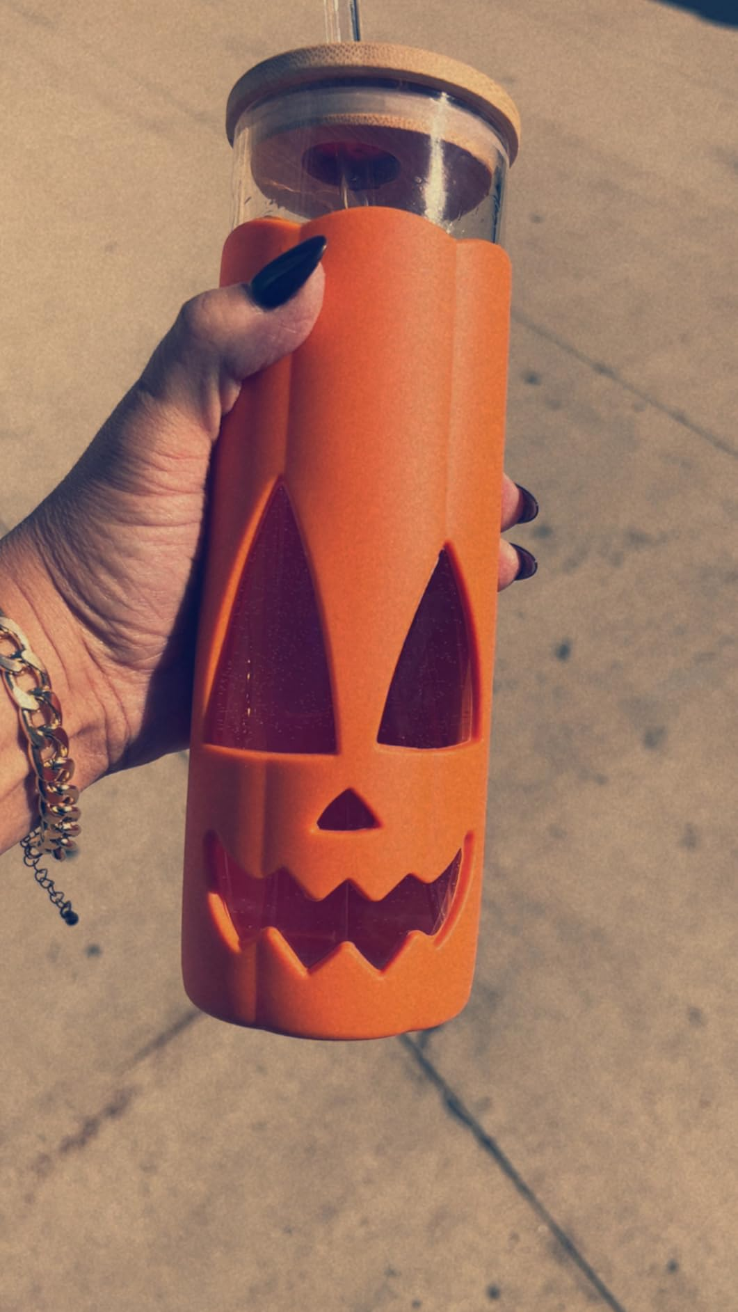 A manus  holds a solid  vessel  with a carved pumpkin design, featuring a bamboo lid and straw, perfect  for Halloween-themed drinks
