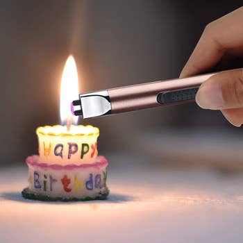 hand using the pink electric lighter to light a candle in the shape of a birthday cake