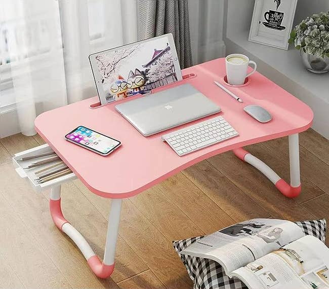 The pink laptop table with electronics and a coffee mug on it