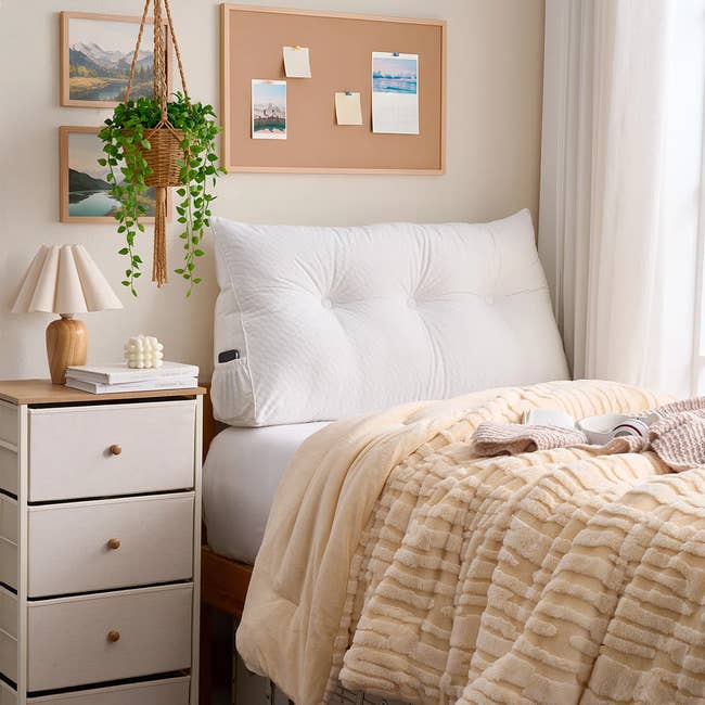 Cozy bedroom with a tufted white headboard, a beige textured blanket, and a small wooden nightstand topped with a lamp and decor