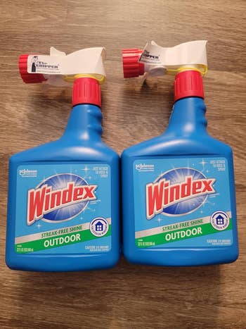 Two bottles of Windex Outdoor spray cleaner with streak-free radiance look connected a woody surface