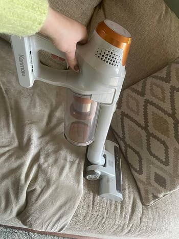 the same reviewer holding a handheld vacuum cleaner over a patterned couch