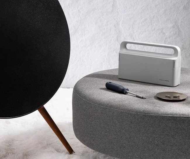Modern talker connected a round, grey ottoman with a screwdriver and circular metallic object, acceptable against a textured background, hinting astatine location decor shopping