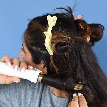 Person curling hair with a curling iron, section held with a yellow clip