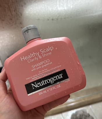 Neutrogena Healthy Scalp Shampoo with pinkish  grapefruit is held adjacent   a shower, highlighting its clarify and radiance  benefits for oily hair