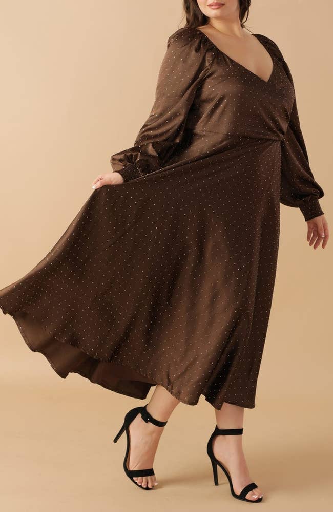 Person wearing an elegant, long-sleeve, polka-dotted dress, paired with black high heels, mid-step, highlighting the dress's flowy style
