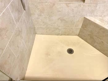 A dirty shower with a yellow floor