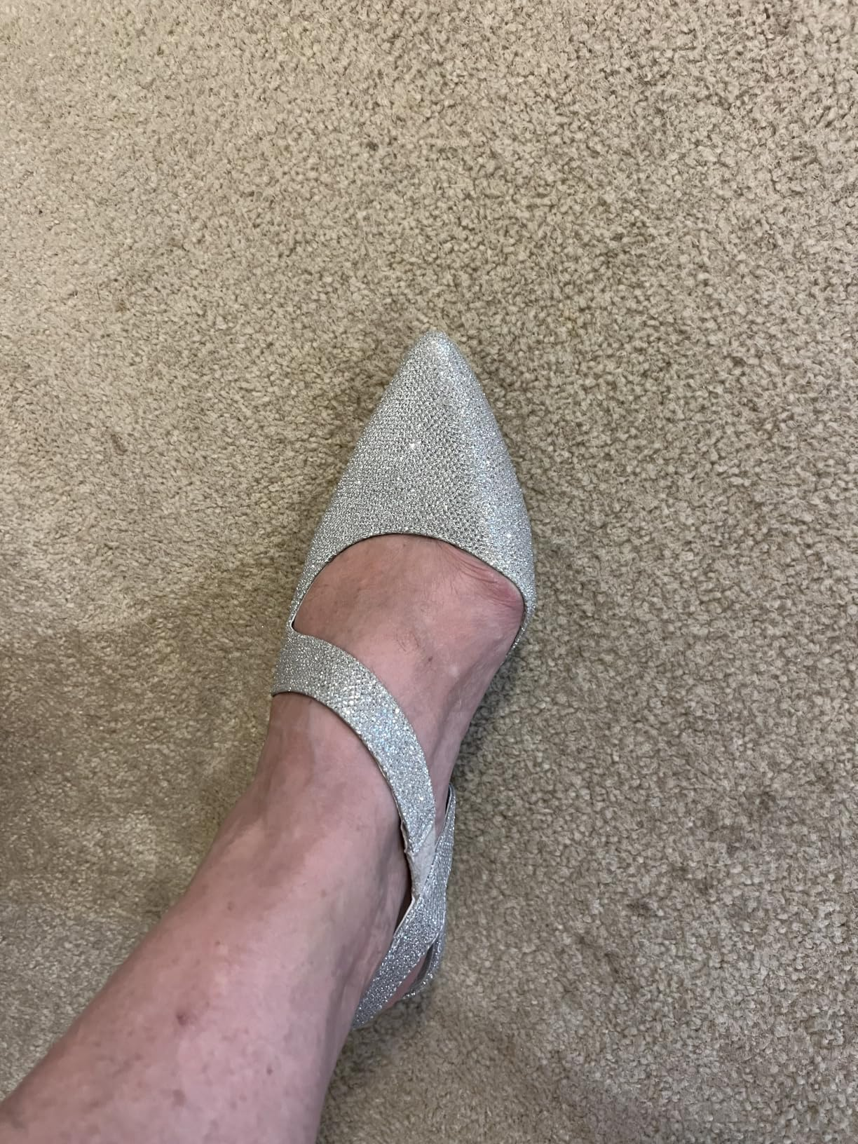 A ft  wearing a sparkly pointed-toe level  footwear  with 2  straps, photographed connected  a textured surface