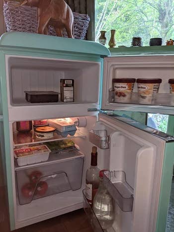 The inside of a reviewer's teal fridge showing the freezer and two shelves and drawer in the fridge
