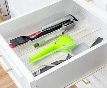 Open drawer with organized room  utensils, including a greenish  peeler, achromatic  and reddish  brush, and a whisk, successful  wide   dividers