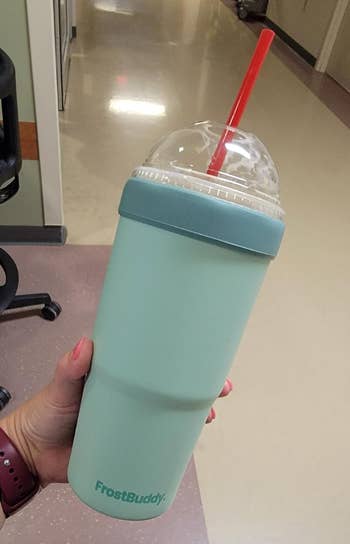 reviewer holding a blue FrostBuddy insulated tumbler with a dunkin cup slid inside of it