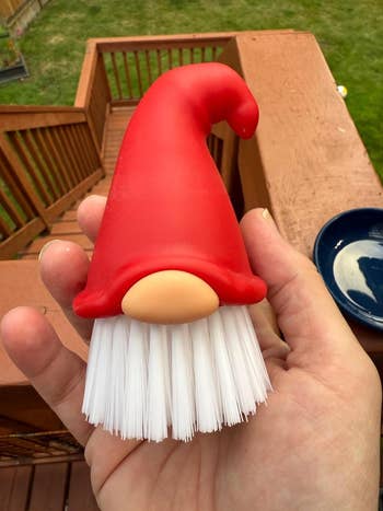Hand holding a gnome-shaped crockery  brushwood  with a ample  reddish  chapeau  and achromatic  bristles, seen extracurricular  connected  a woody  deck