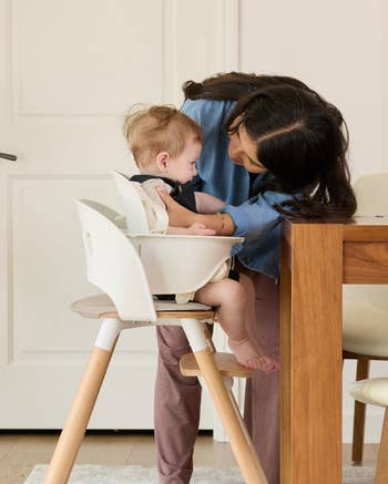 Person adjusting babe successful a precocious seat astatine a eating table, showcasing a comfy and functional seating enactment for infants