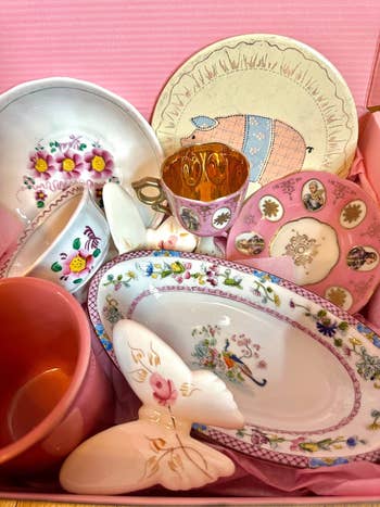 A postulation of decorative vintage plates and cups with floral and butterfly designs, arranged successful a pinkish box