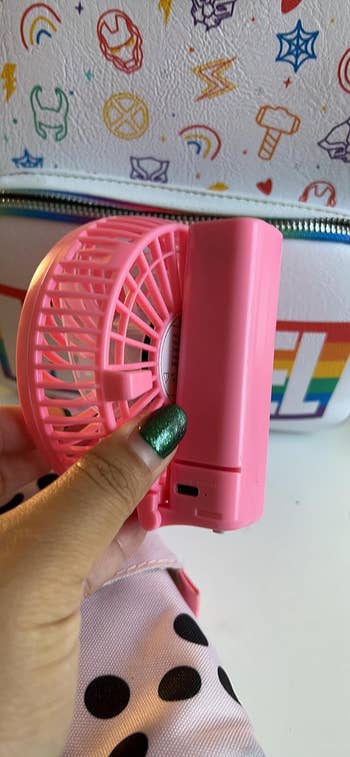 Hand holding a portable pink fan with the handle folded up so it's compact