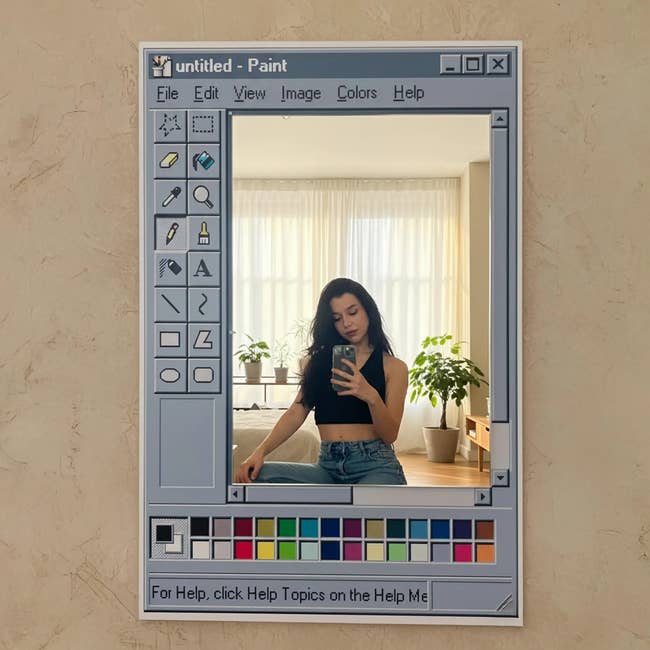 Person taking a reflector selfie with a retro bundle interface frame, wearing a achromatic apical and jeans, surrounded by indoor plants