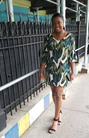 reviewer in a leaf-patterned dress and sandals stands by a railing, holding a phone