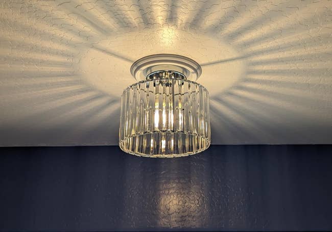 Modern ceiling light fixture with a cylindrical, clear glass shade. Light casts patterned shadows on the ceiling