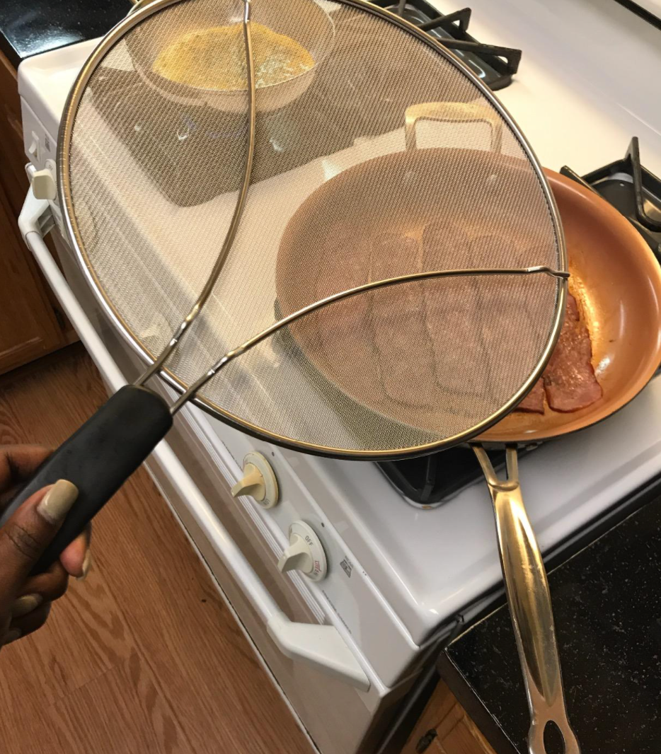 Reviewer holding up a splatter screen over a frying pan full of bacon 
