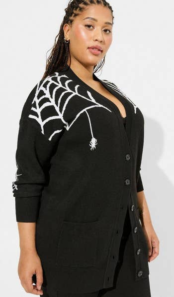 A model wearing a black cardigan with spider web graphics on the shoulders 