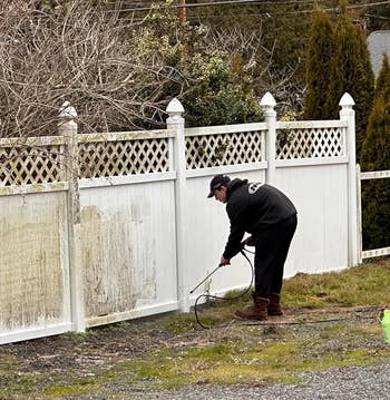 Person power washing a dirty fence
