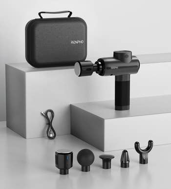 Massage gun with four attachments, charging cable, and carrying case displayed on a minimalist surface