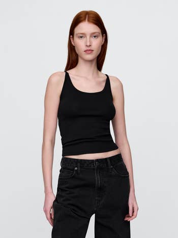 A idiosyncratic   wearing a achromatic  vessel  apical  and acheronian  jeans poses with hands successful  pockets against a plain background