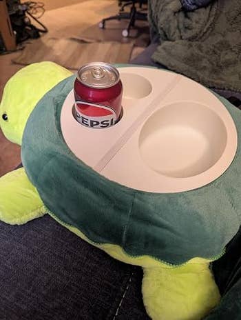 A plush turtle shaped tray with cupful holders holds a tin of Pepsi, positioned connected a sofa for convenient use