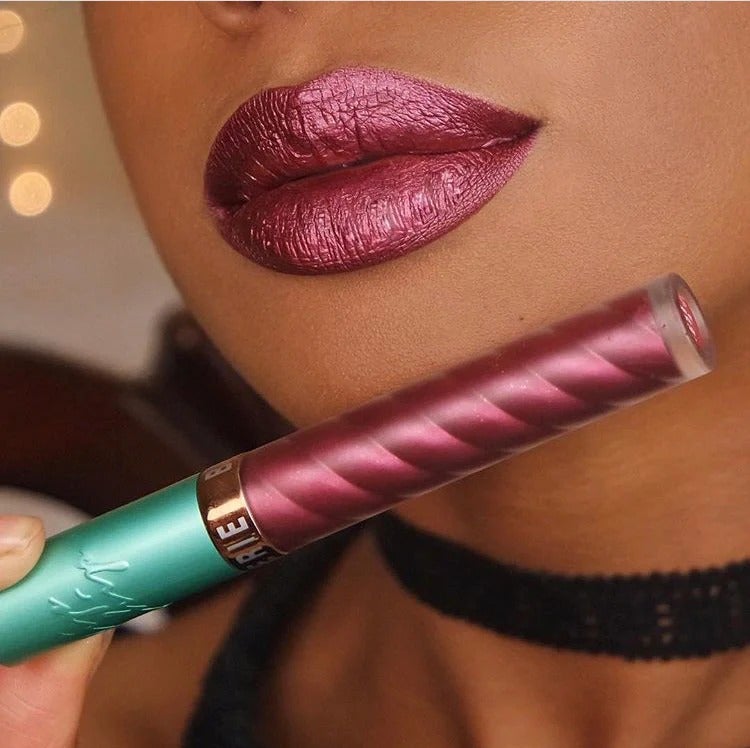 a model wearing the red metallic liquid lipstick and holding up the tube
