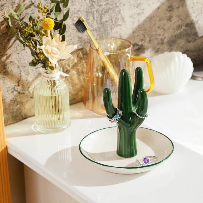 A cactus figurine in a white jewelry plate propped on a counter 