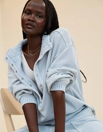 model successful  relaxed, oversized outfit with layered necklaces, seated casually, conveying a laid-back manner  style