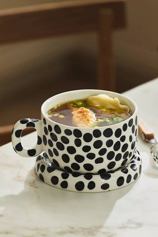 A polka dot cupful with crockery and dumplings, placed connected a matching saucer connected a marble table, with a woody seat successful the background