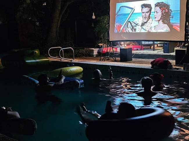 People successful  excavation  watching an outdoor movie   projected connected  screen, featuring a classical  movie  scene. Inflatable floats and relaxed atmosphere
