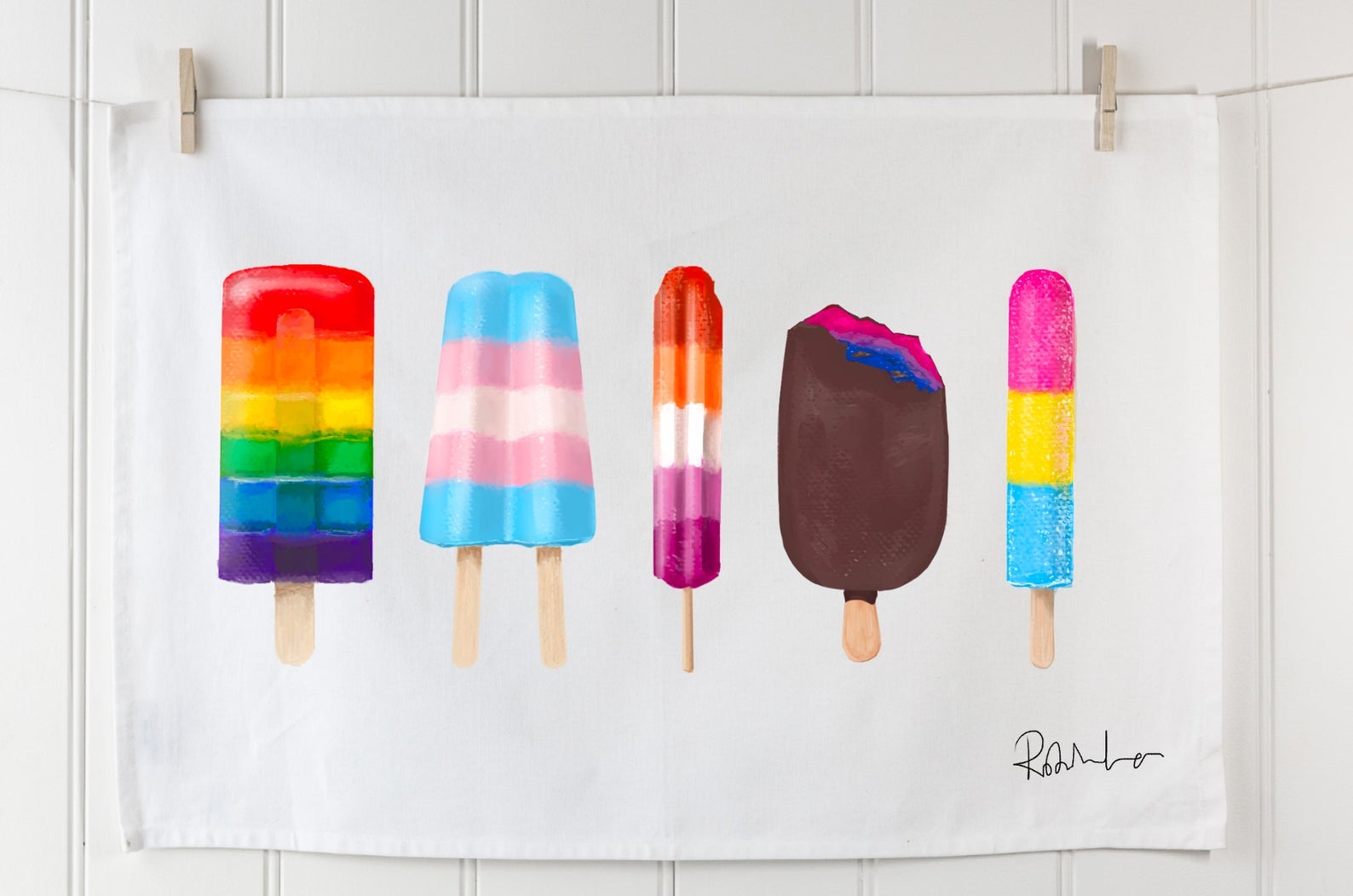 white tea towel with illustrations of popsicles with various pride flag prints and the artist's signature in black in the bottom right corner