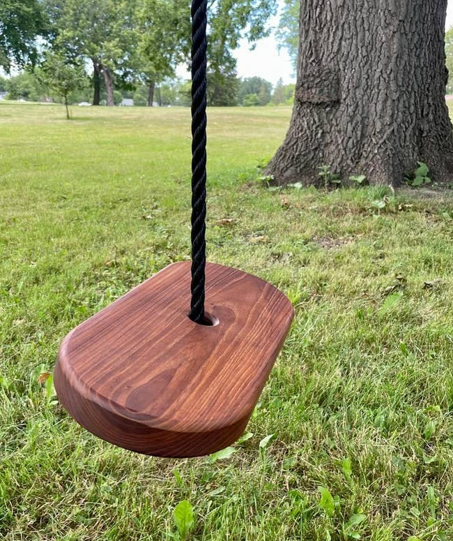 a wooden tree swing with a rope fed through the center of the oval-shaped seat 