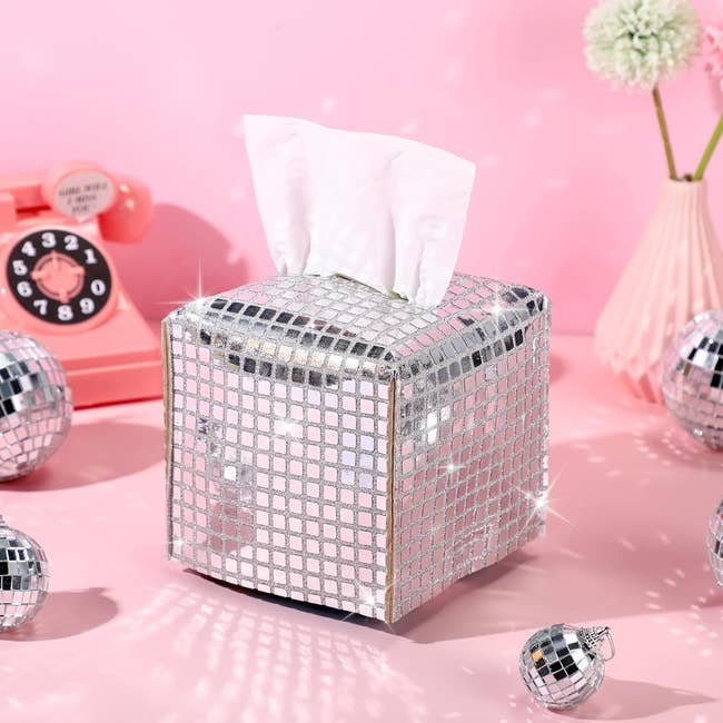 Tissue box with a shiny, reflective sequin-like cover, surrounded by disco balls and retro decor