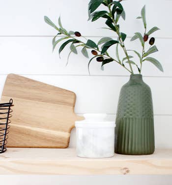 Wooden cutting board, white ceramic jar, and a textured green vase with a plant